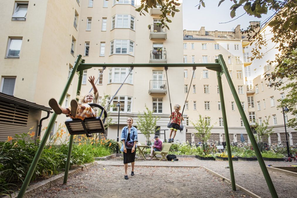 Children swing on a swing in the courtyard, a woman pushes the children